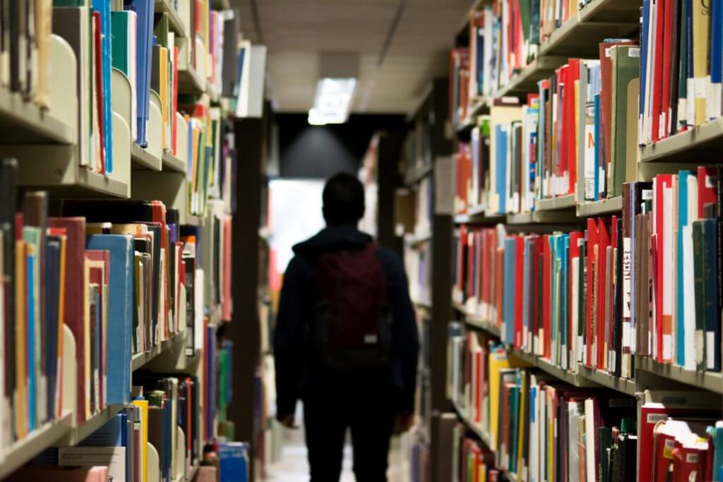 A student walking through stacks of books in a library