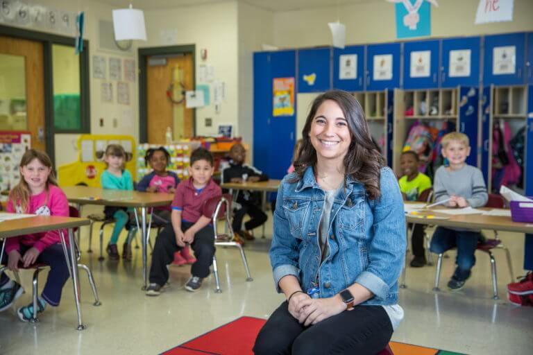 Photo of a college-age female student teacher with in her DeKalb Public Schools classroom, with young students seated behind her.